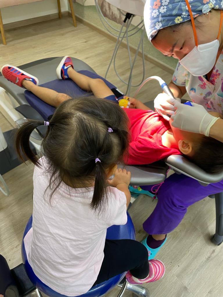 Supportive sibling at just kids dental clinic singapore. Sister watches brother during dental checkup.